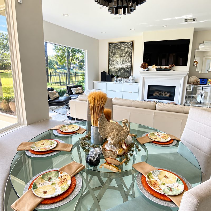 Bright living room with a glass dining table set for autumn, a fireplace and a garden view