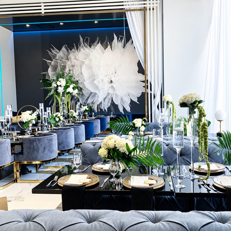 Dining room with a giant white paper flower, black and gold place settings and white floral centerpieces